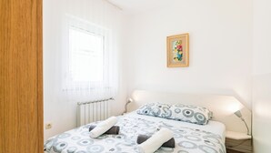 A bedroom with a bed, a window with curtains, a bedside lamp, and a framed picture on the wall. - Apartment for 2 persons with sea view (Crikvenica)