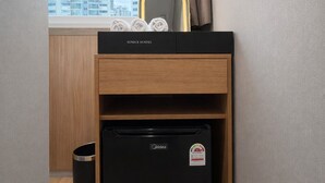 Une petite cuisine équipée avec un réfrigérateur noir, un meuble de rangement en bois et une fenêtre avec des rideaux.