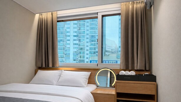 Une chambre d’hôtel comprenant un lit, une table de chevet avec un miroir, un petit réfrigérateur et une fenêtre avec des rideaux.