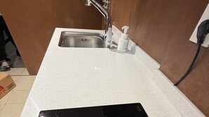 Une cuisine dotée d’une plaque de cuisson à induction noire, d’un évier en acier inoxydable et d’un plan de travail blanc.