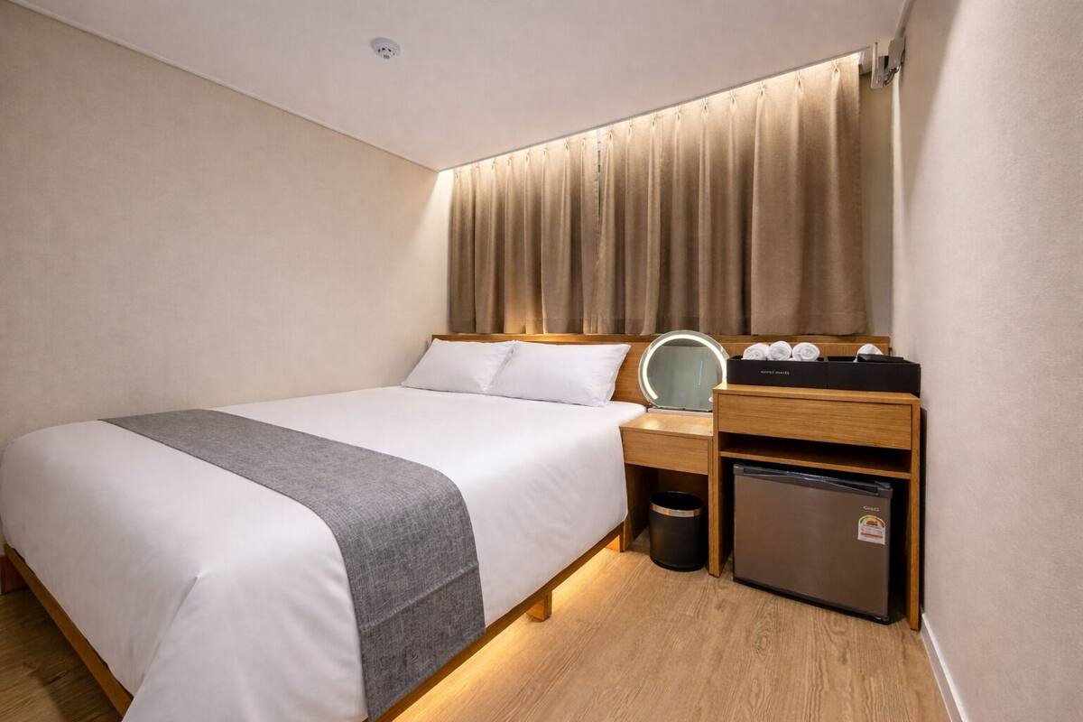 A hotel room with a bed, bedside table, mirror, and a small refrigerator.