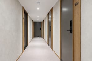 Een gang met deuren genummerd 202 en 204, een lichtkleurig tapijt en een plafond met inbouwverlichting.