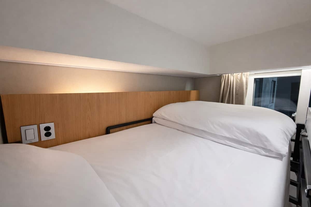 A hotel room with two beds, a wooden headboard, a window with curtains, and a bedside table.