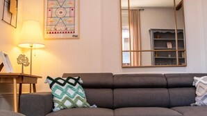 A living room with a sofa, a glass coffee table, a lamp, and a mirror. - Particulier rémois proche Cathédrale avec parking et terrasse (Reims)