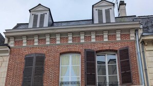 A two-story building with a brick facade, a large wooden door, and a window with shutters. - Particulier rémois proche Cathédrale avec parking et terrasse (Reims)