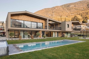 A modern multi-story building with a swimming pool, outdoor seating, and a mountainous backdrop. - Trianglhof Apartment 'Bozen' Southwest View and Private Garden (Bolzano)