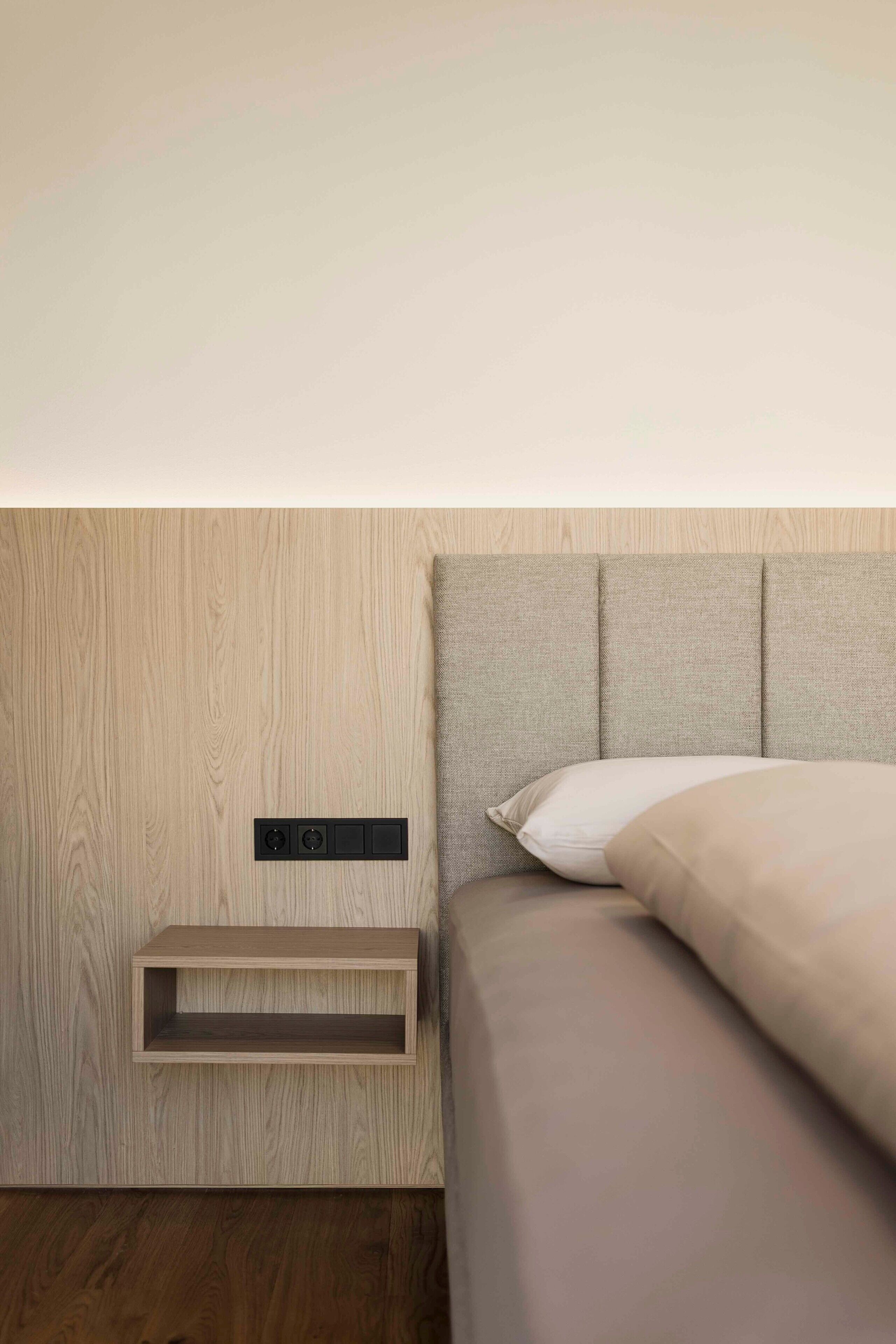 Une chambre moderne avec un mur en bois, une étagère intégrée et un lit doté d’une tête de lit grise.