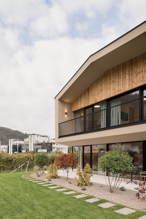 Ein modernes Gebäude mit Holzfassade, großen Fenstern und einem gepflegten Garten mit trittfesten Steinen.