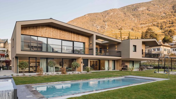 A modern multi-story building with a swimming pool, outdoor seating, and a mountainous backdrop. - Trianglhof Apartment 'Kampill' with Stunning Mountain Views and Spacious Balcony (Bolzano)