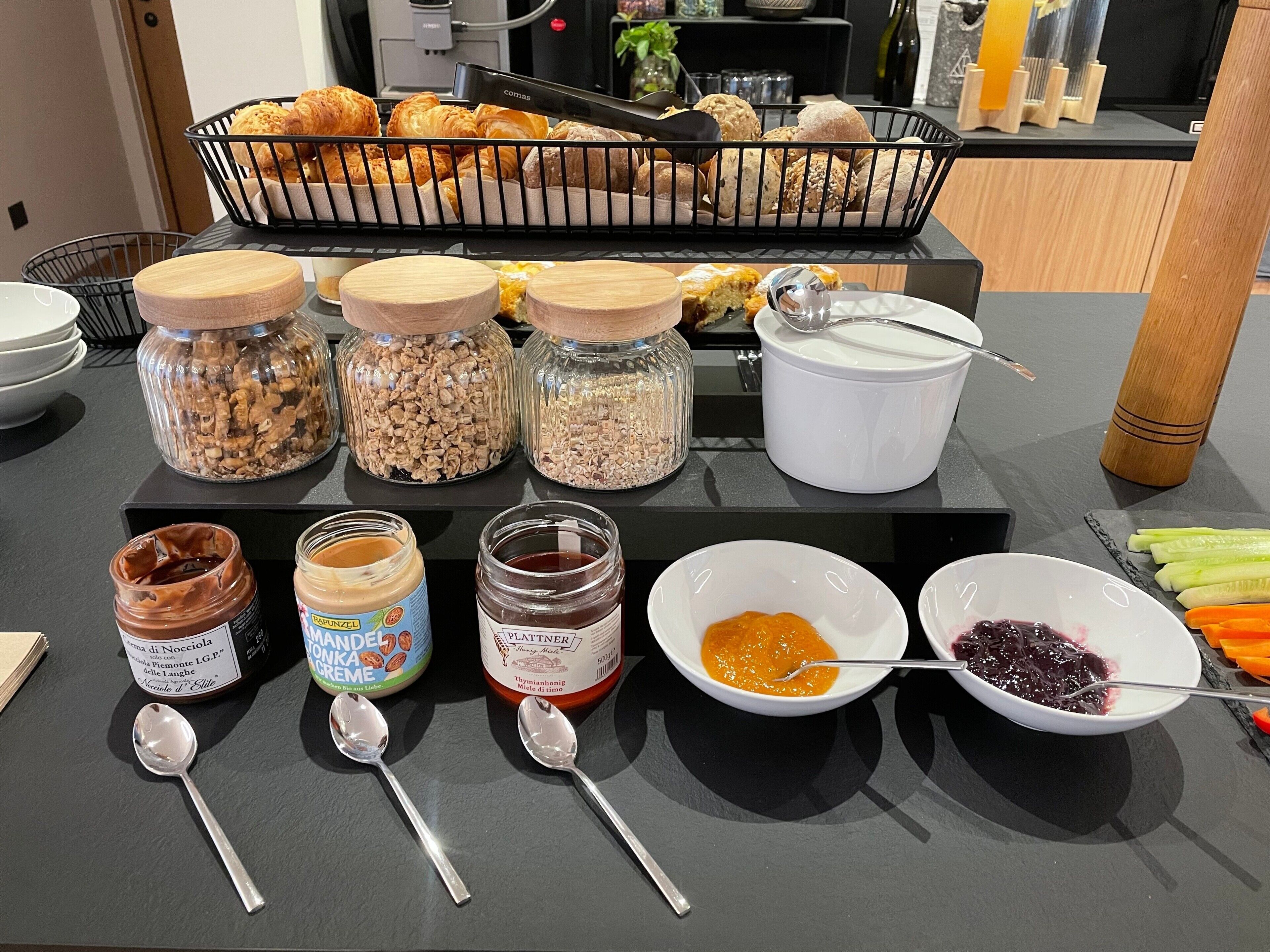 A breakfast buffet with various pastries, granola, jams, and spreads.