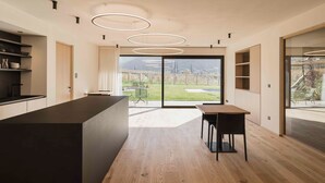 A modern kitchen with a large island, built-in shelves, and a view through large glass doors. - Trianglhof Apartment 'Hörtenberg' with Spacious Balcony and Southwest View (Bolzano)