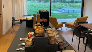 A modern dining area with a long table, chairs, and a view of a vineyard through large windows. - Trianglhof Apartment 'Hörtenberg' with Spacious Balcony and Southwest View (Bolzano)