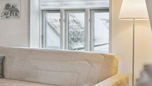 A living room with a beige sofa, a lamp, and a window with a view of a snowy landscape. - 4 Star Holiday Home in Oksbol (Oksbol)