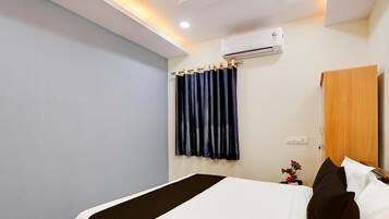 Una habitació d'hotel amb un llit, una nit de nit amb un ram de flors, un armari de fusta i una unitat de climatització a la paret.