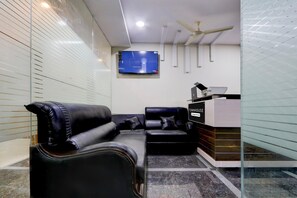 Una hall moderna con un divano in pelle nera, un pannello di vetro, un televisore a schermo piatto montato a parete e una ventola a soffitto.
