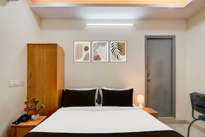 Una camera d'albergo con un letto, un comodino, una lampada, una sedia e un'opera d'arte appesa al muro.
