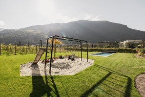 A backyard with a swing set, a sandbox, and a pool. - Trianglhof Apartment 'Rosengarten' with Mountain View and Rooftop Terrace (Bolzano)