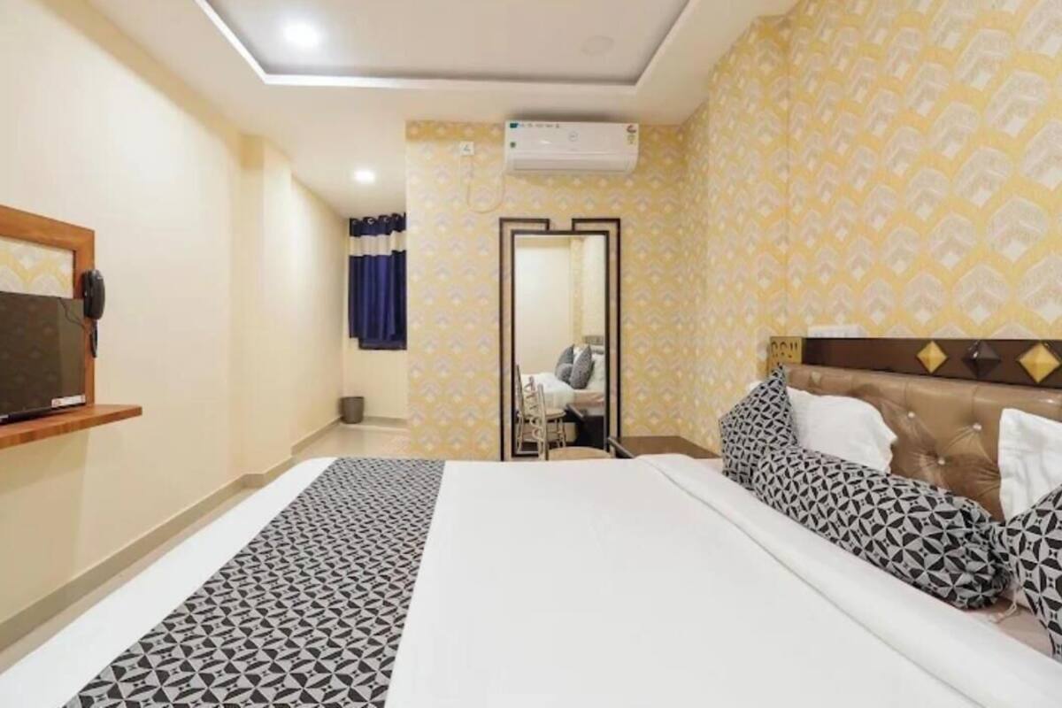 A hotel room with a bed, a TV mounted on the wall, and an air conditioning unit.