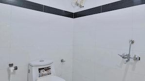 Une salle de bain avec des carreaux blancs, des toilettes, une douche et un porte-serviettes.