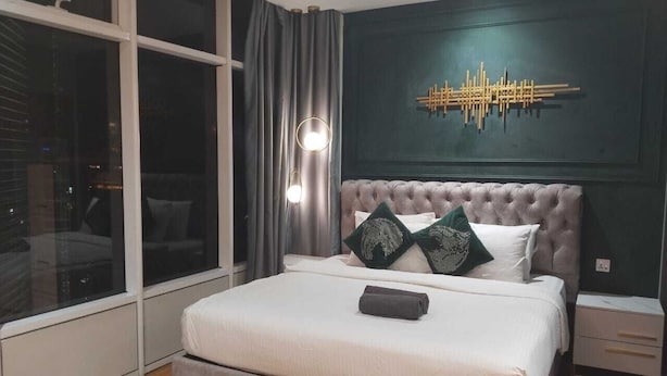 Een slaapkamer met een groot raam, een gestuufd hoofdeinde en een wandlamp.