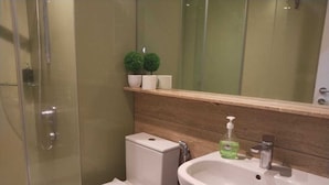 Een badkamer met een glazen douchecabine, een wit toilet, een wastafel met zeepdispenser en een spiegel boven de wastafel.