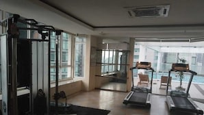 Een fitnessruimte met trainingsapparatuur, een loopband en uitzicht op een zwembad.