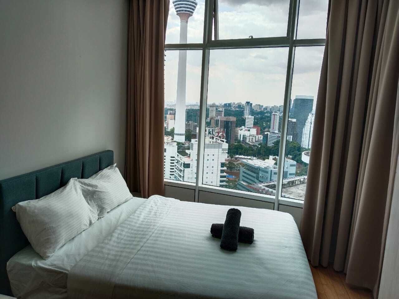 A hotel room with a large window, a bed with white linens, and a view of a cityscape.