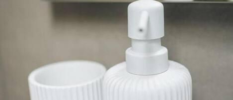 Un dispensador blanco con textura acanalada y una taza blanca sobre una superficie blanca.