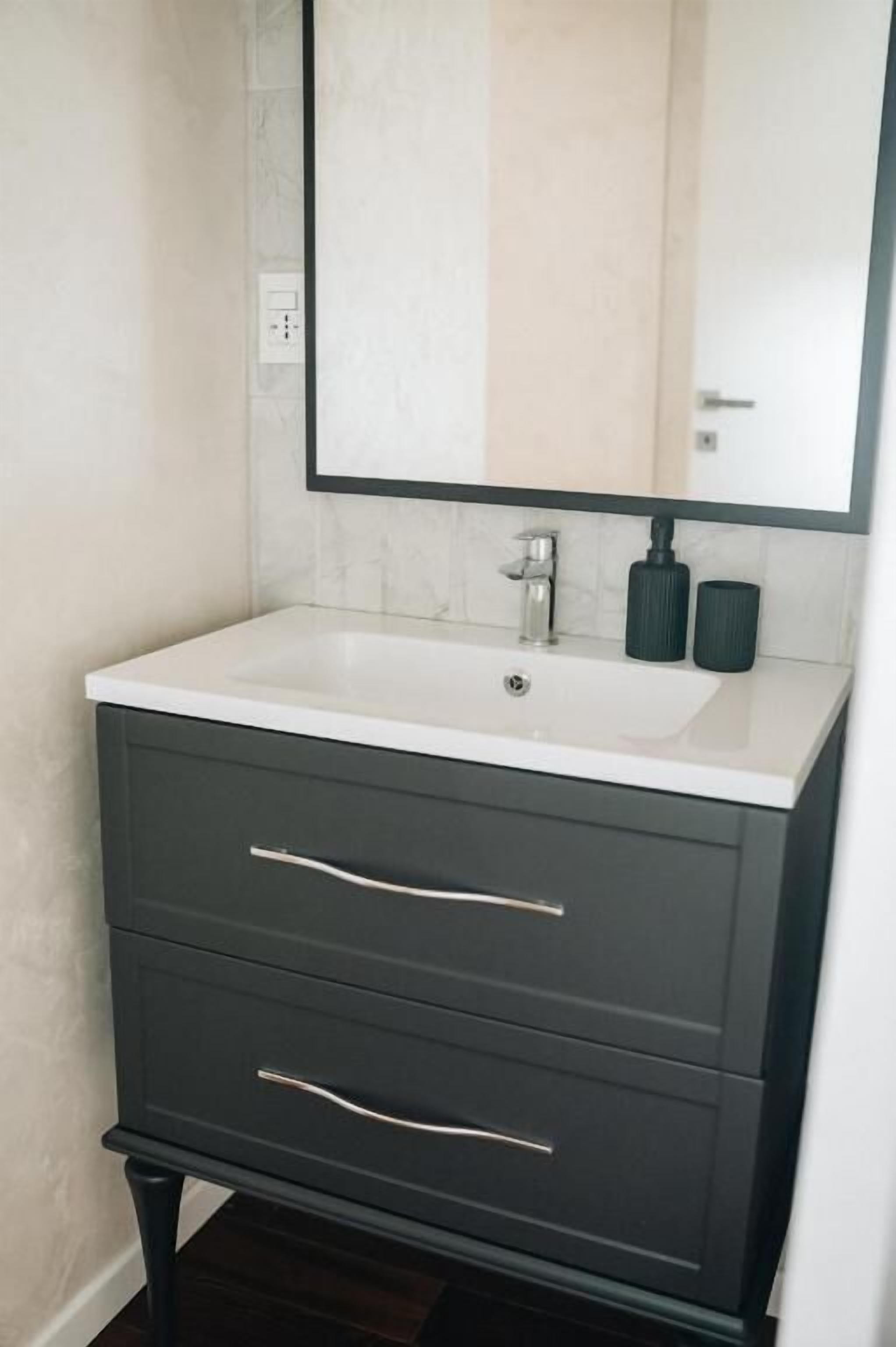A bathroom with a white sink, dark cabinet drawers, a black faucet, and a large mirror.