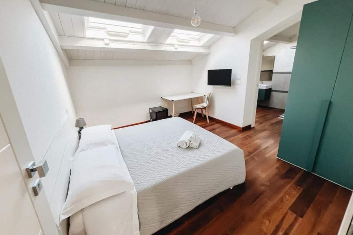 A bedroom with a bed, a desk, a chair, and a TV.