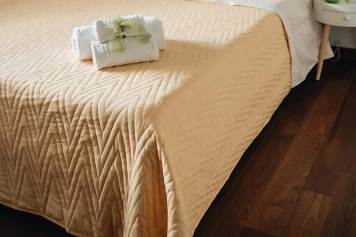 A neatly made bed with a beige quilt, a folded towel on the bed, and two bedside lamps on nightstands.