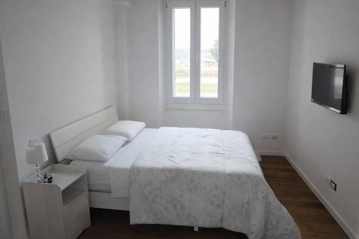 A bedroom with a bed, a nightstand, a TV mounted on the wall, and a window.