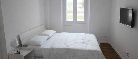 A bedroom with a bed, a nightstand, a TV mounted on the wall, and a window.