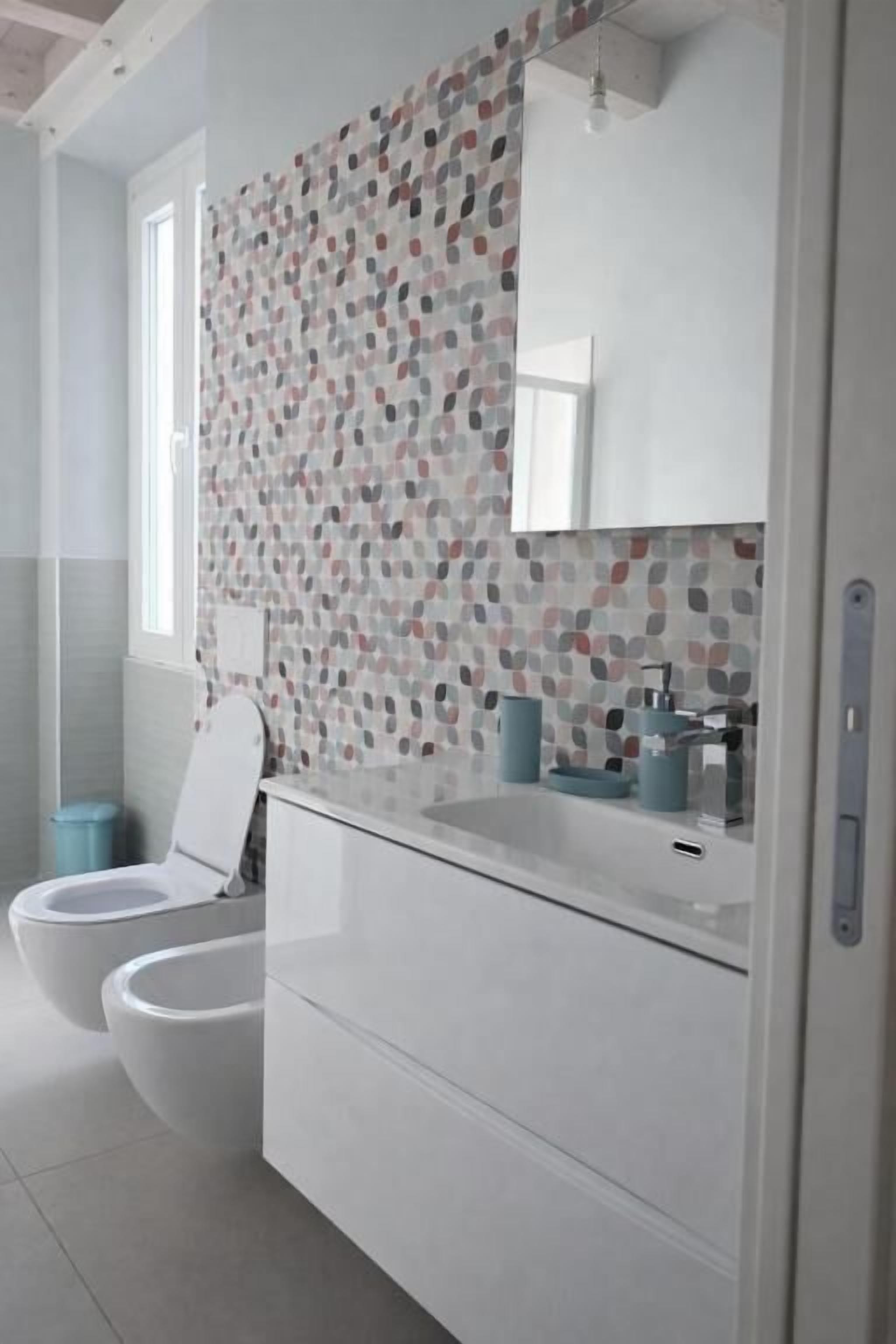 Un baño moderno con pared estampada, un lavabo blanco y dos inodoros.
