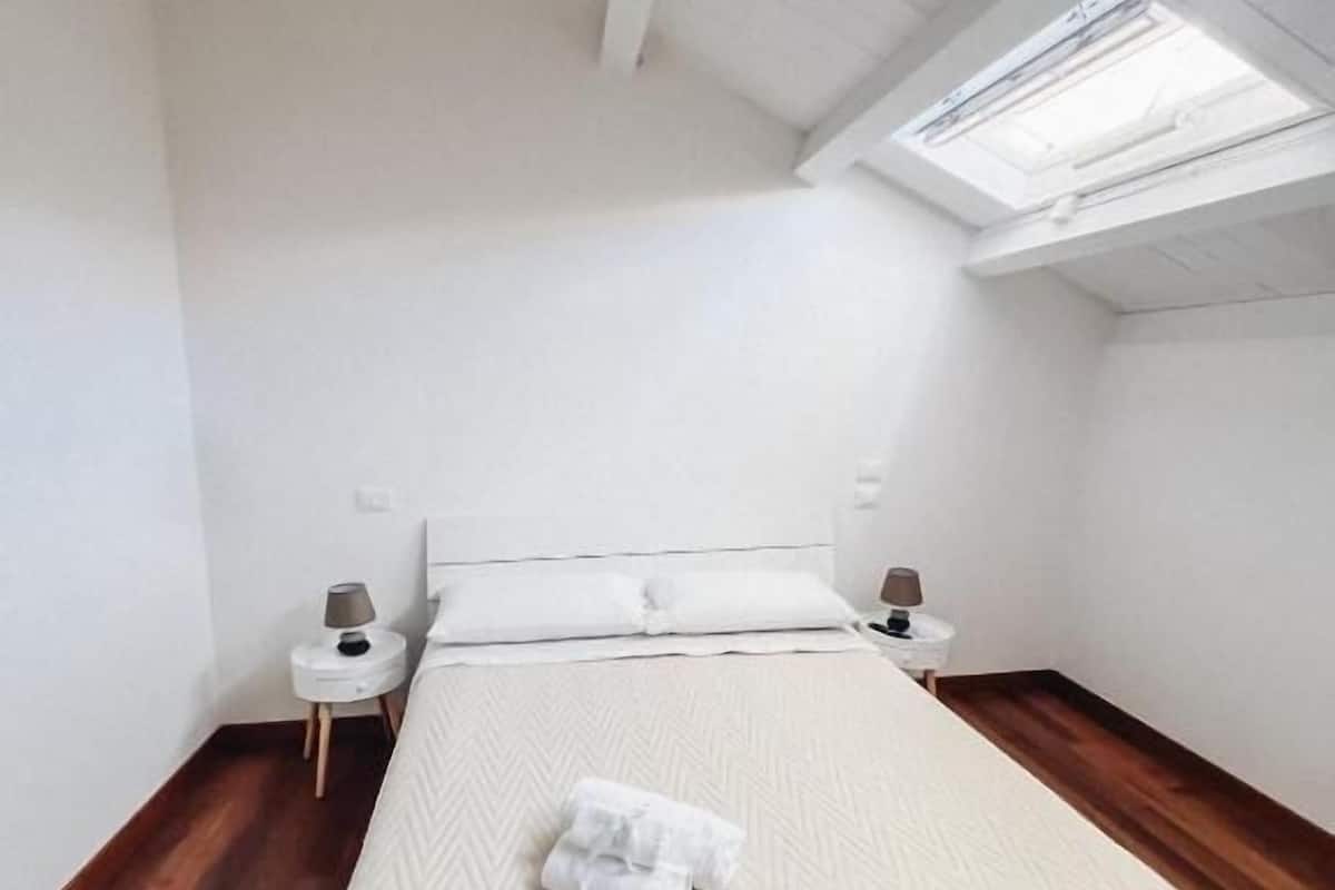 A bedroom with a bed, two bedside tables, a skylight, and wooden flooring.