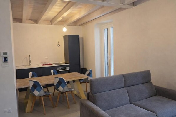 Une cuisine moderne avec une table et des chaises, un canapé gris et une fenêtre avec des stores.