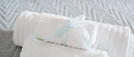 Deux serviettes pliées avec soin, maintenues par un ruban bleu clair, reposent sur un couvre-lit à motifs.