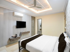 A hotel room with a bed, a TV, a desk with a chair, a mirror, and a ceiling fan.