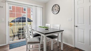 Een eetgedeelte met een tafel, stoelen, een klok en uitzicht door een glazen deur.