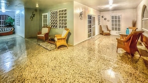 A spacious room with a polished floor, a seating area with chairs, a wall-mounted artwork, and a door leading to another room. - Casa Nube (Caguas)