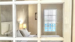 A room with a bed, a window with bars, a lamp, and a door. - Casa Nube (Caguas)