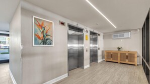 An interior with three elevators, a painting, and a wooden console. - Ocean Sands 2-602 (Madeira Beach)