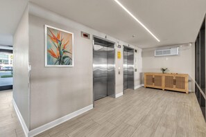 An interior with three elevators, a painting, and a wooden console. - Ocean Sands 2-602 (Madeira Beach)
