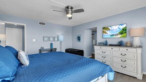 A bedroom with a bed, a ceiling fan, a dresser, a television, and a wall-mounted picture. - Ocean Sands 2-602 (Madeira Beach)