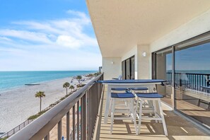 Ein Balkon mit Tisch und Stühlen mit Blick auf einen Strand, Palmen und einen klaren Himmel.