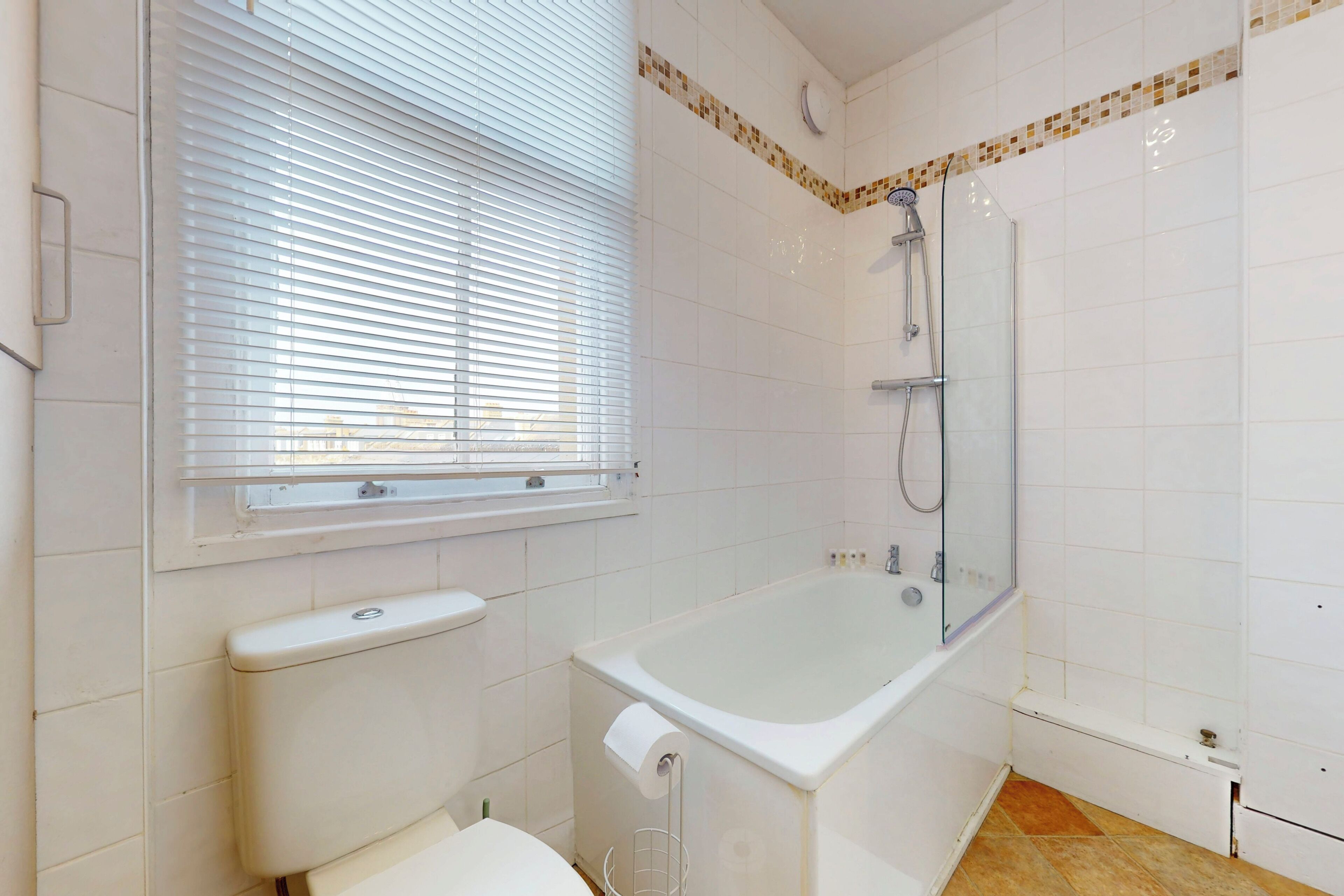 A bathroom with a toilet, a bathtub, a shower, and a window with blinds.
