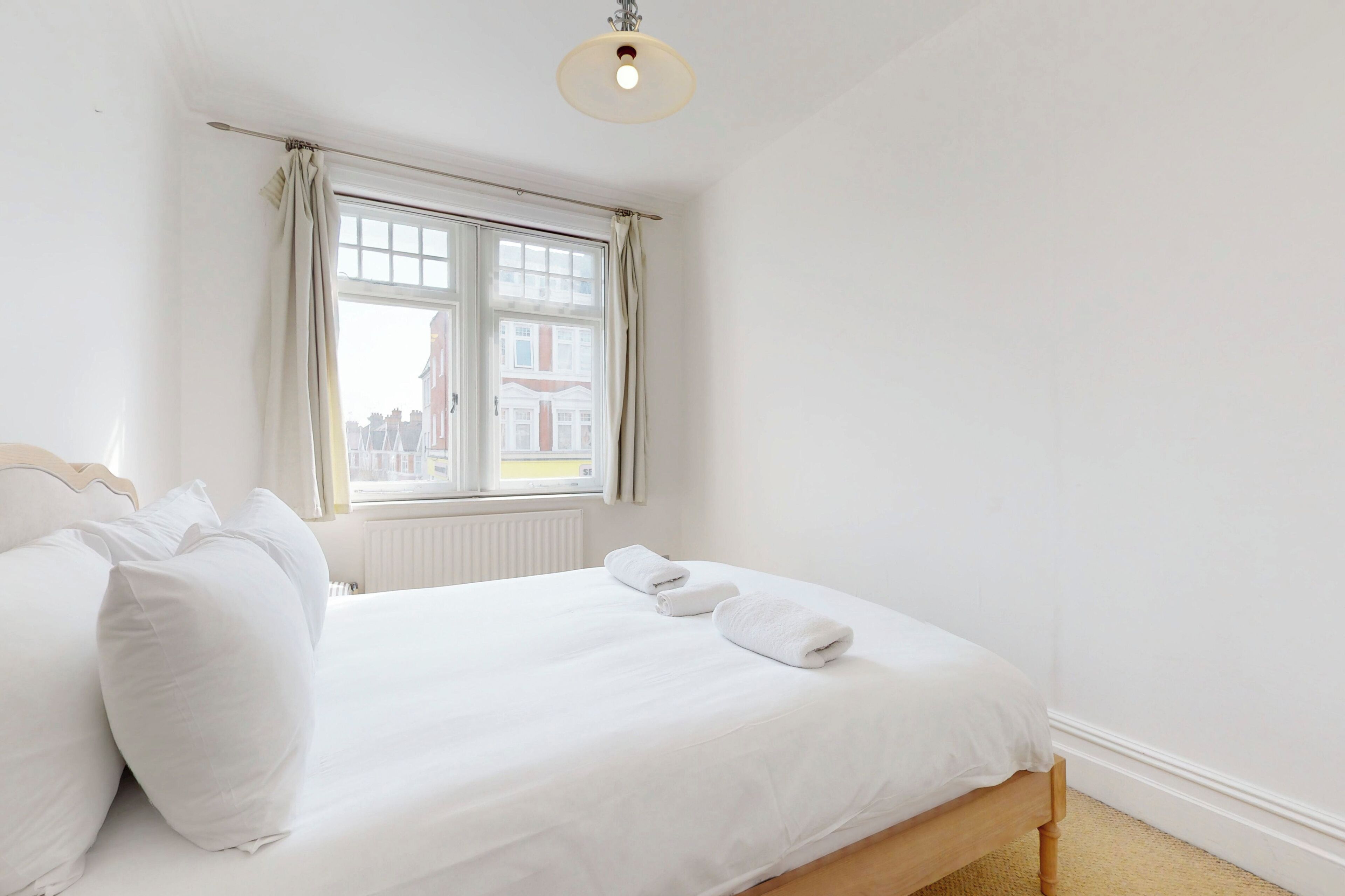 A bedroom with a bed, white curtains, a window, and a radiator.