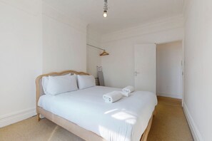 A bedroom with a bed, a hanging towel rack, and a door leading to another room. - Bright 2BR Wimbledon Home Near Centre Court & Tube (London)