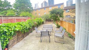 A patio with outdoor furniture, a wooden fence, and a view of tall buildings in the background. - London Luxe 5-bed House Retreat (London)