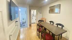 A dining area with a table and chairs, a TV mounted on the wall, a radiator, and a kitchen in the background. - London Luxe 5-bed House Retreat (London)